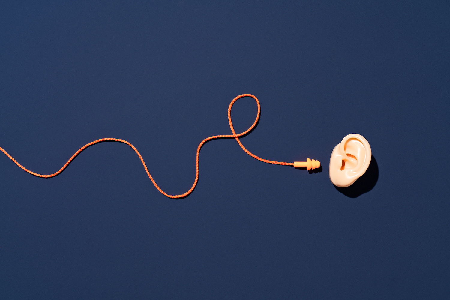 Orange earbuds with curved cord Reach to ear on blue background directly above view.  4 tips for RevOps teams to filter out the noise and focus on the big picture